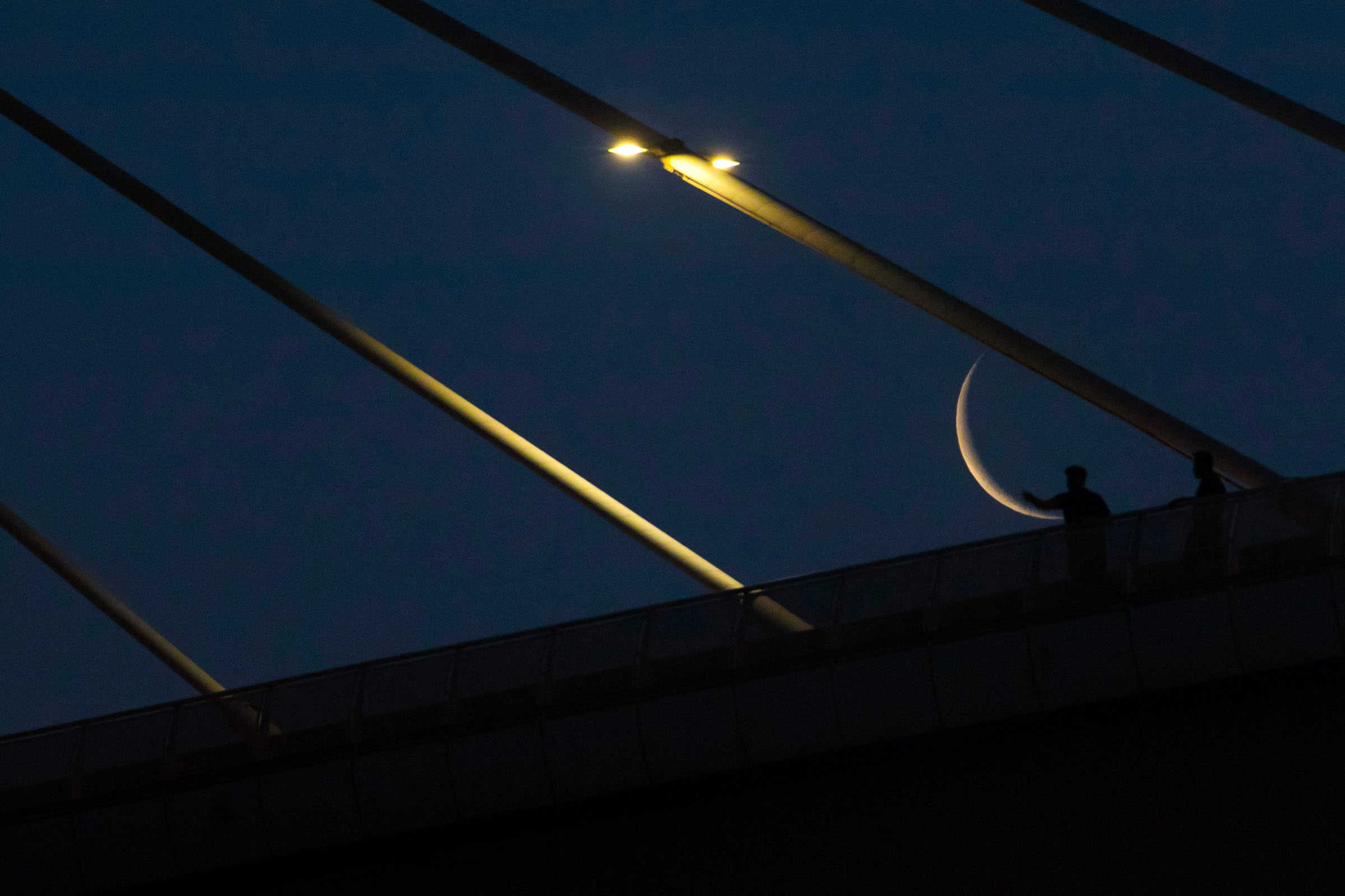 The waning crescent moon, near the end of the Muslim holy month of Ramadan, is pictured behind the Mohammad Baqir al-Sadr bridge in Iraq's southern city of Basra early on April 28, 2022. (Photo by Hussein Faleh / AFP)