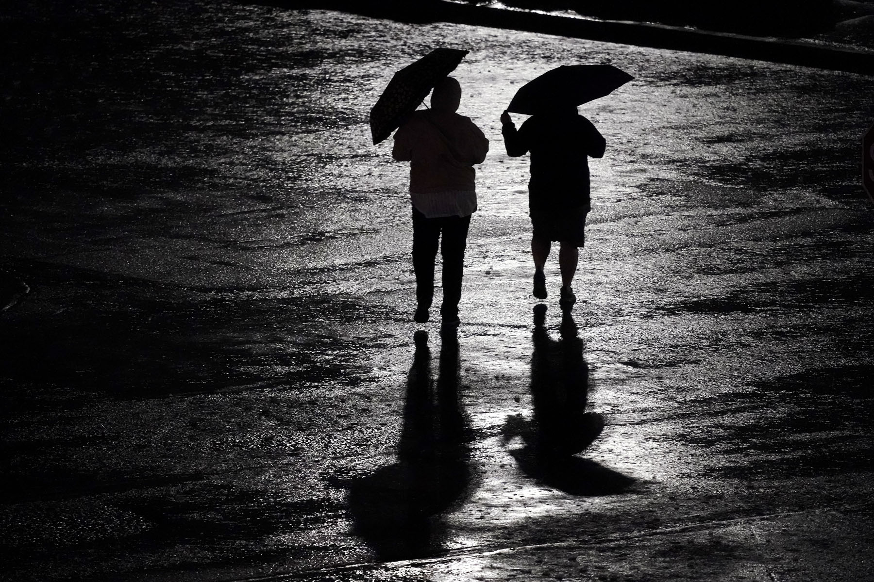 People walk across a rain-soaked parking lot after a baseball game between the Kansas City Royals and the New York Yankees Friday, April 29, 2022, in Kansas City, Mo. The game was called after eight innings due to weather. (AP Photo/Charlie Riedel)