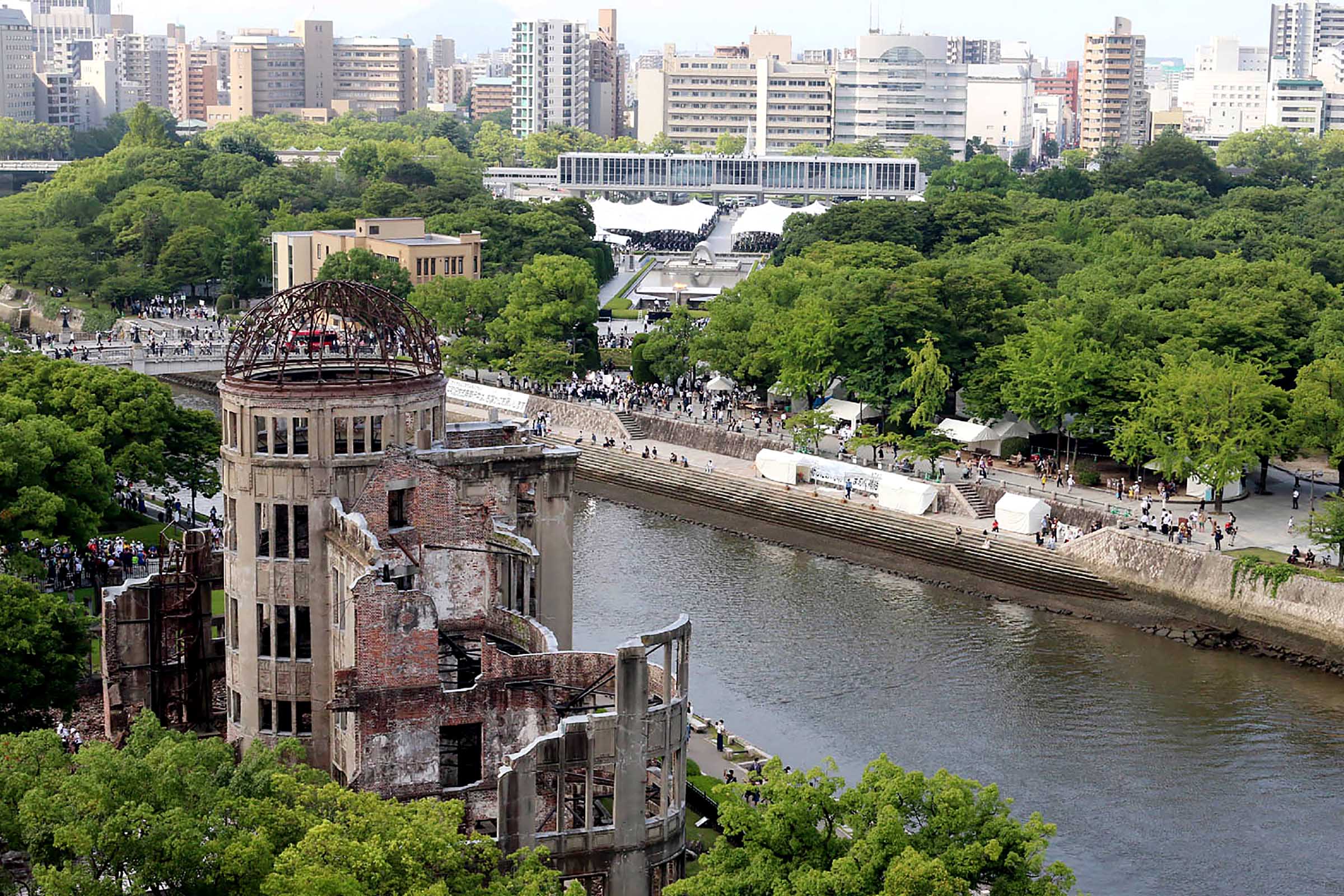 People walk along the water across from the Atomic Bomb Dome (L) as others attend the annual memorial ceremony at the Hiroshima Peace Memorial Park (back C) in Hiroshima on August 6, 2022, to mark 77 years since the world's first atomic bomb attack. (Photo by JIJI PRESS / AFP) / Japan OUT