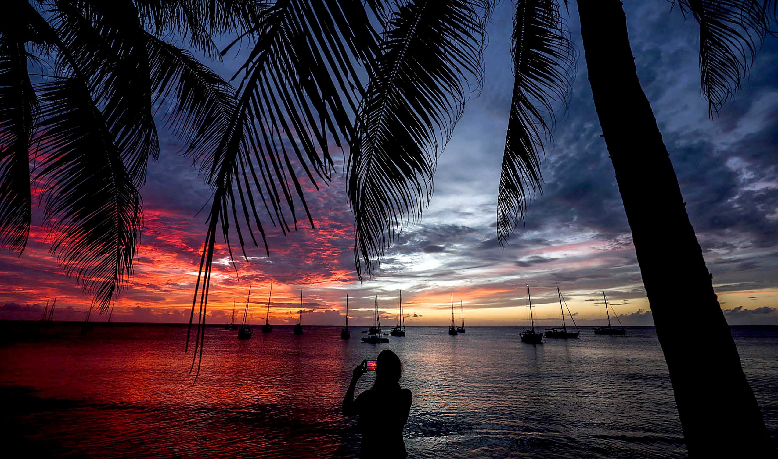 A woman takes photographs of the ocean during the sunset in Le Carbet, on the French Caribbean island of Martinique on November 24, 2022. (Photo by Charly TRIBALLEAU / AFP)