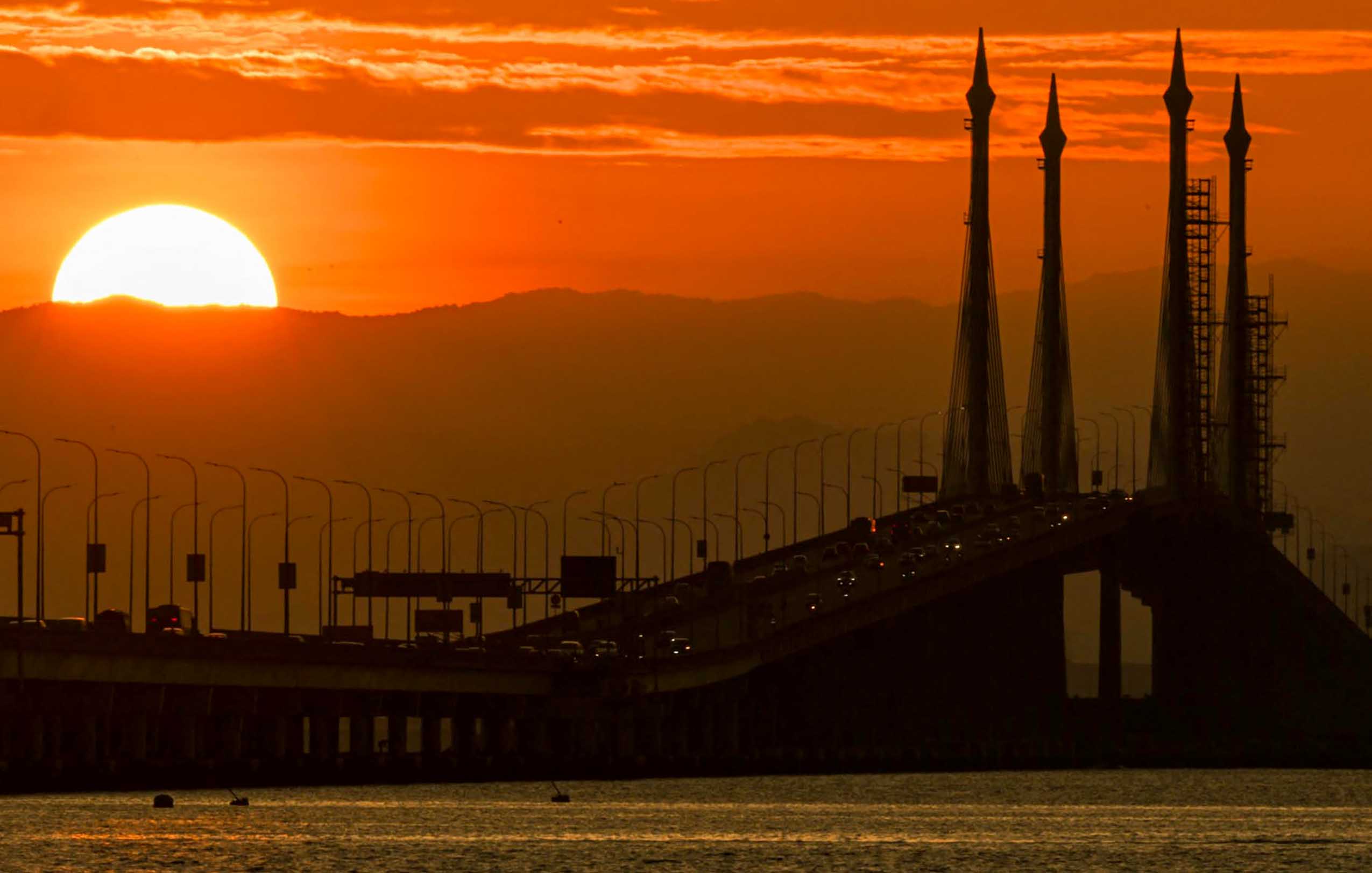 The sun rises as motorists cross over the Penang Bridge in George Town on Malaysia's Penang Island on March 11, 2023. (Photo by Mohd RASFAN / AFP)